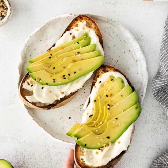 avocado toast on a plate with a hand holding it.