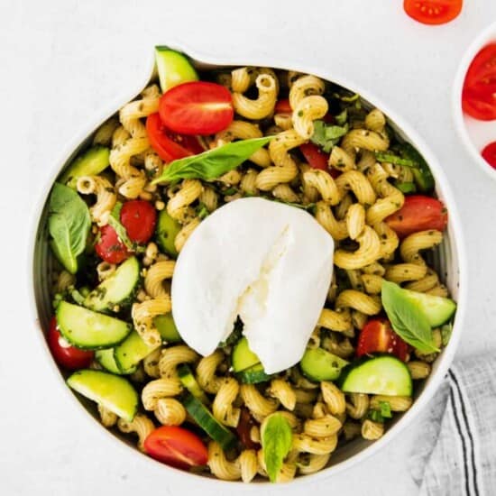 a bowl of pasta salad with tomatoes, basil and mozzarella.