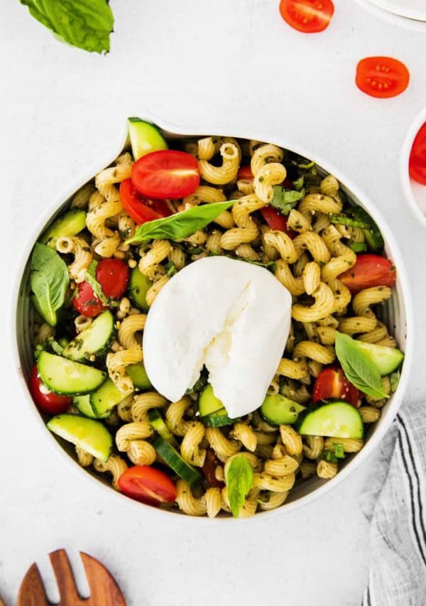 a bowl of pasta salad with tomatoes, basil and mozzarella.