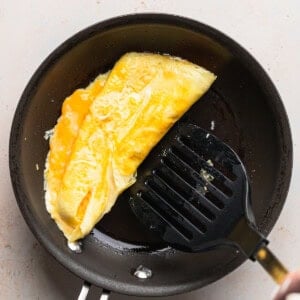 a person cooking a cheese omelette in a frying pan.