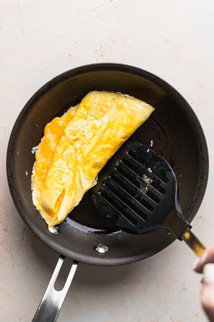 cheese omelette being folded with a spatula in a skillet