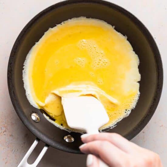 a person making a cheese omelette with a spatula in a frying pan.