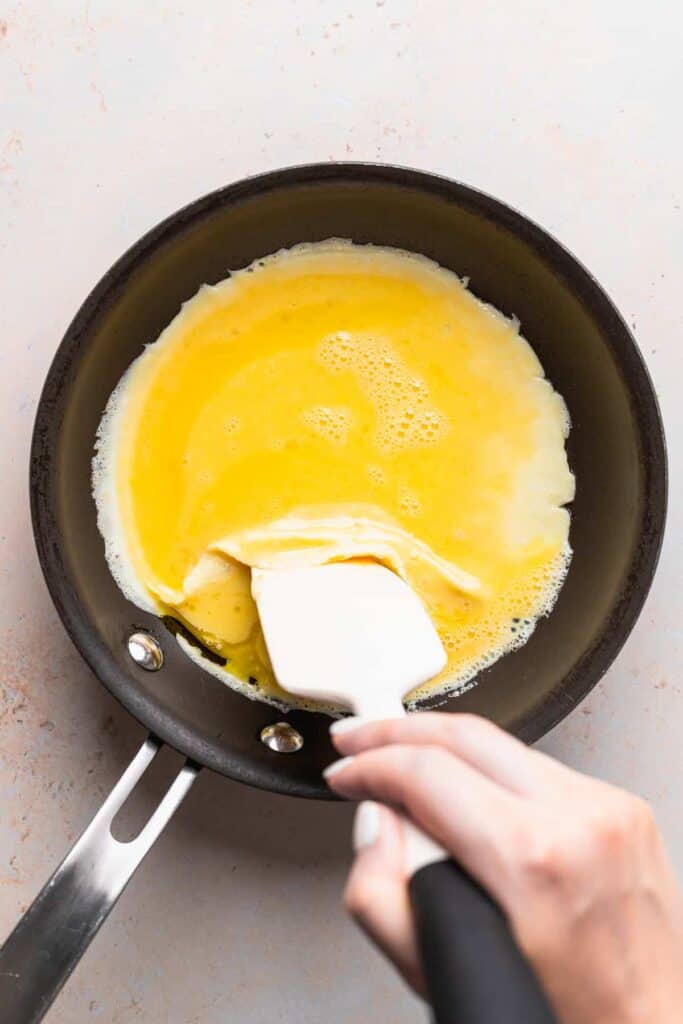 The start of a cheese omelette in a skillet being folded by a spatula.