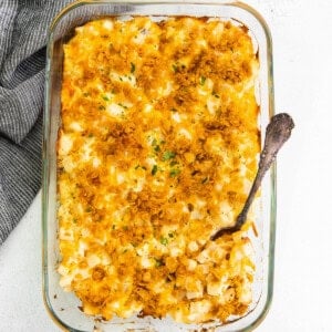 Cheesy hashbrown potato casserole served in a glass dish with a fork.