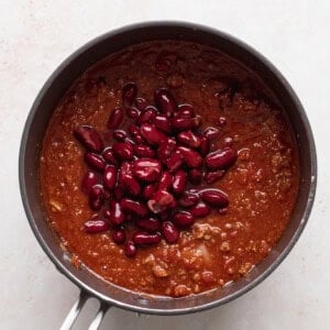 chili beans atop a bed of crispy fries, all served in a pan on a white surface.