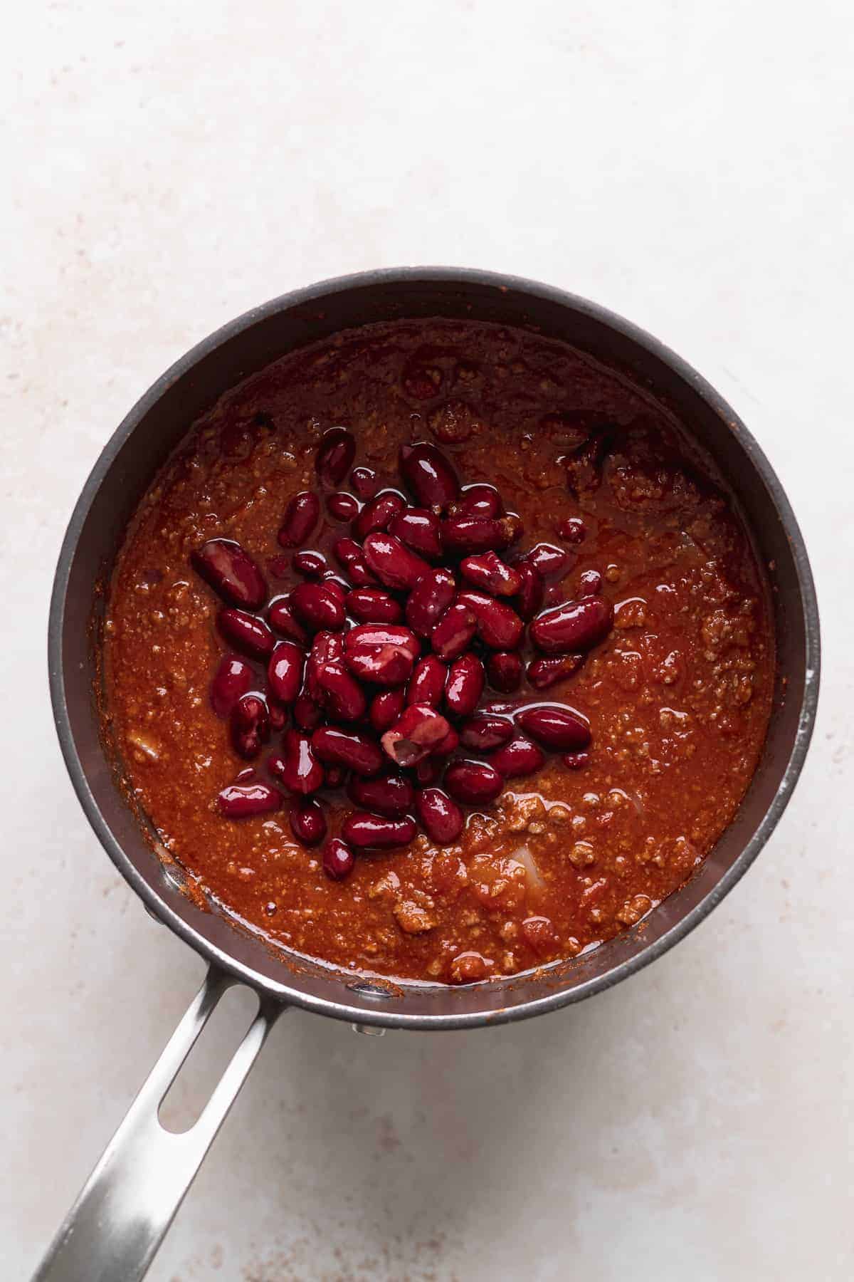 chili beans atop a bed of crispy fries, all served in a pan on a white surface.