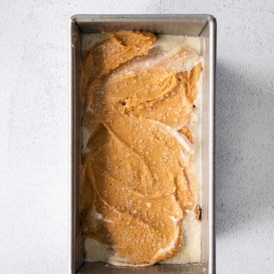 A pumpkin cream cheese bread baked in a pan with a layer of icing.