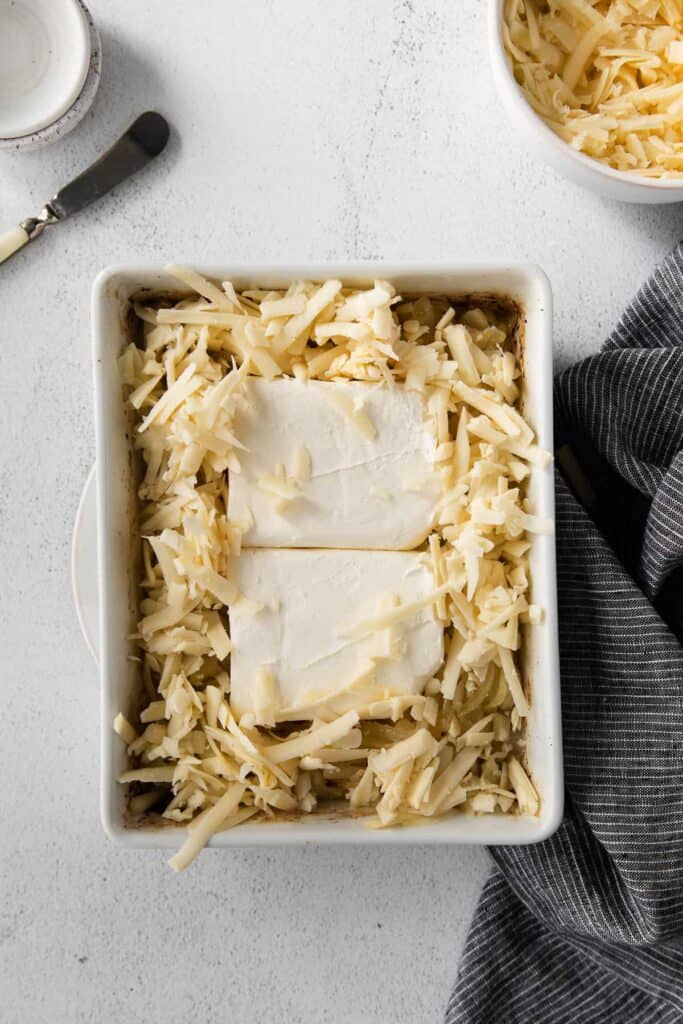 Cream cheese and shredded cheese in a casserole dish for french onion dip.