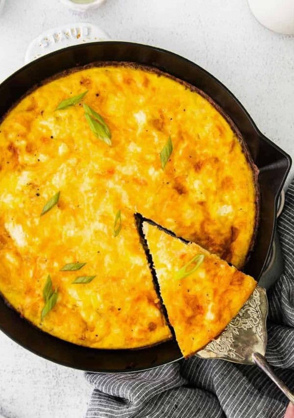 a slice of four cheese frittata being removed from cast iron skillet