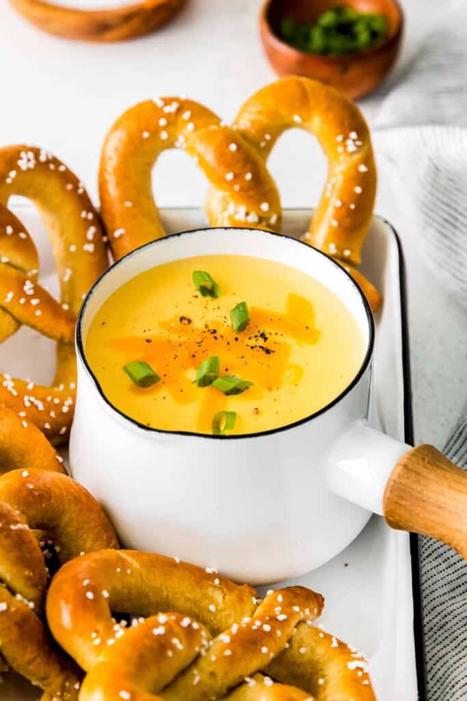 A saucepan full of beer cheese dip surrounded by soft pretzels. 
