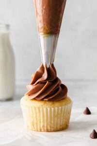 a chocolate frosting being poured onto a cupcake.