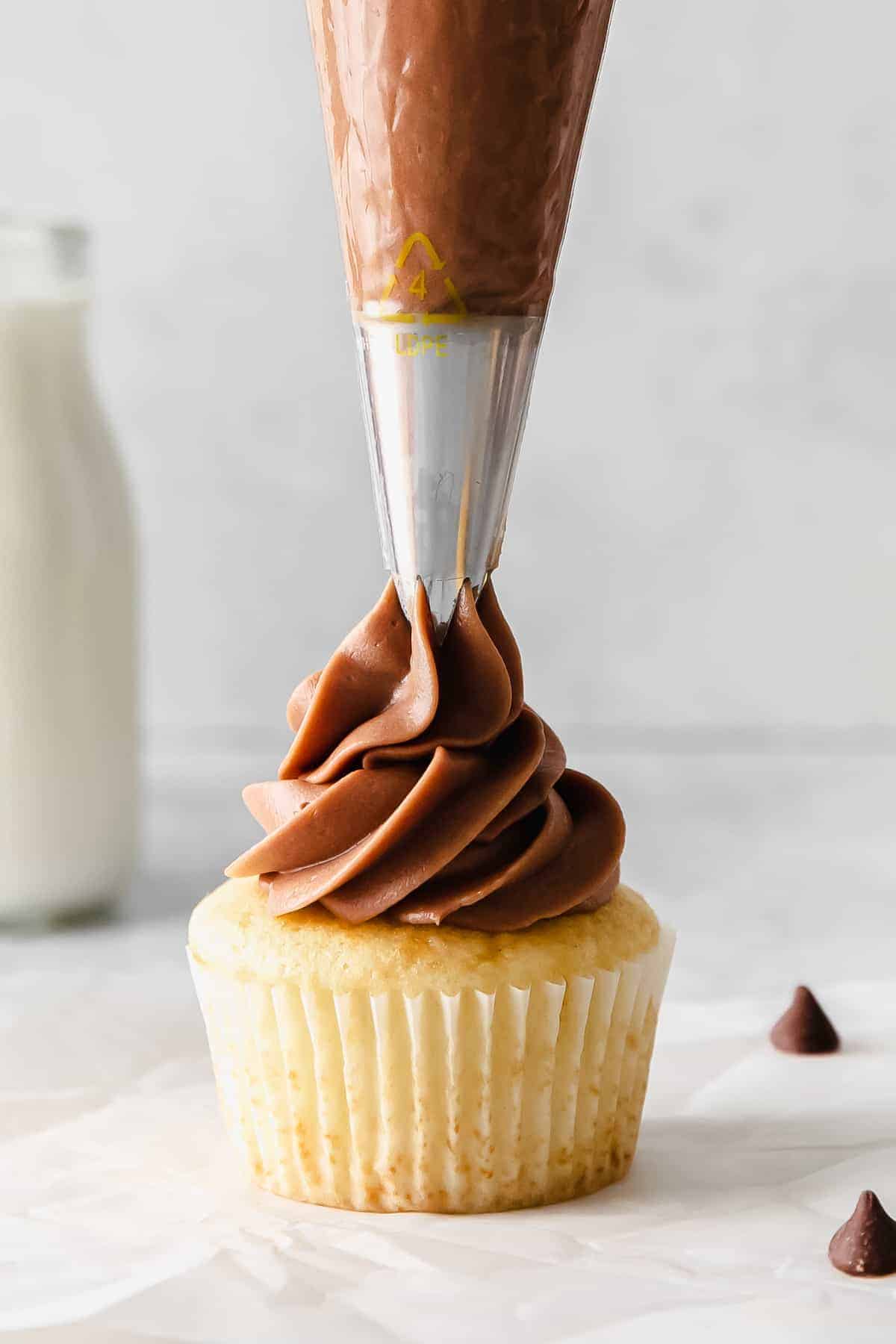 Pipping cream cheese frosting on top of a cupcake. 