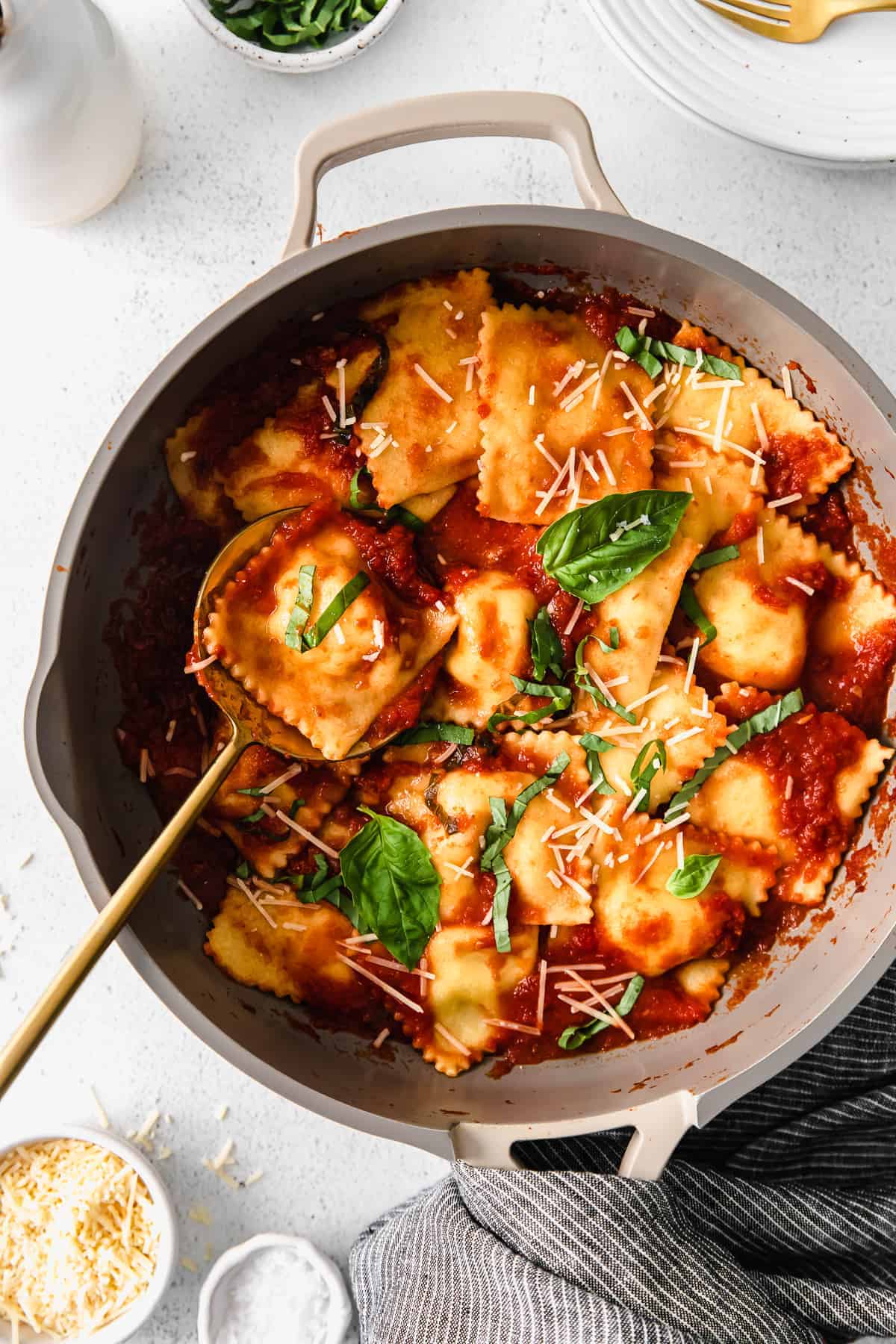 homemade cheese ravioli in a skillet topped with marinara and fresh basil