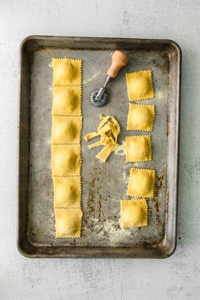 homemade cheese ravioli cut with a pasta knife on a baking sheet