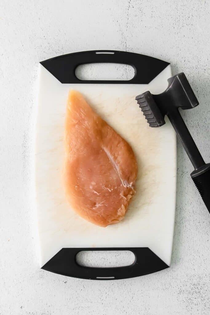 chicken breast on a cutting board with a tenderizing mallet