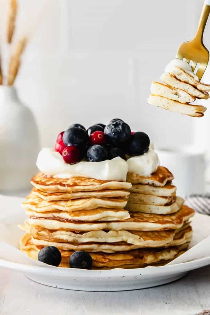 stack of cream cheese pancakes topped with berries and yogurt