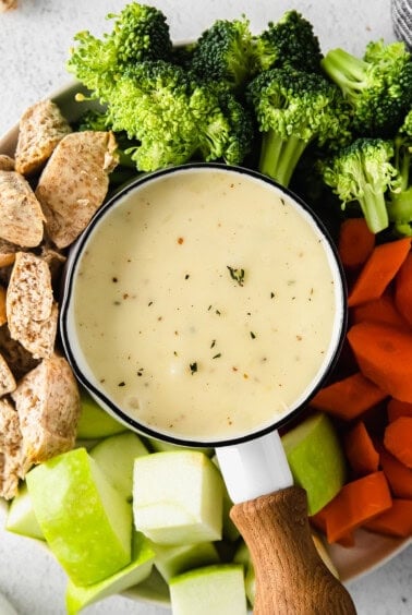 Cheese fondue surrounded by vegetables and bread.
