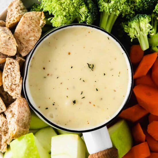 Cheese fondue surrounded by vegetables and bread.