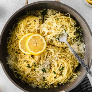 pasta in a pan with lemon slices and parmesan cheese.