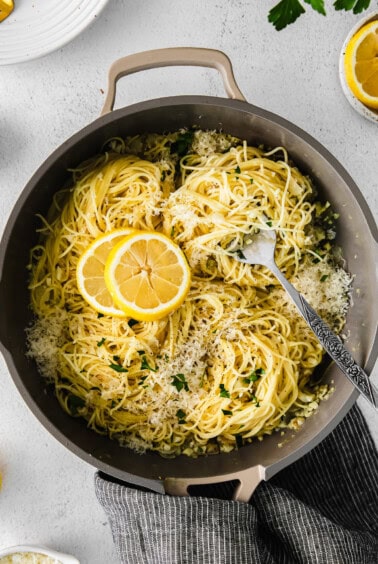 pasta in a pan with lemon slices and parmesan cheese.