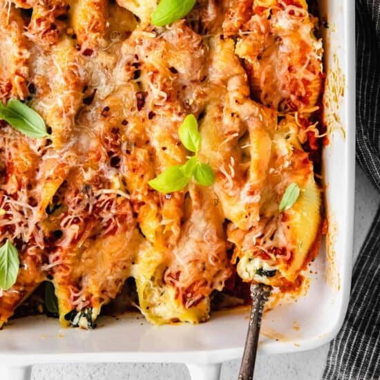 Ricotta stuffed shells with basil leaves in a white baking dish.