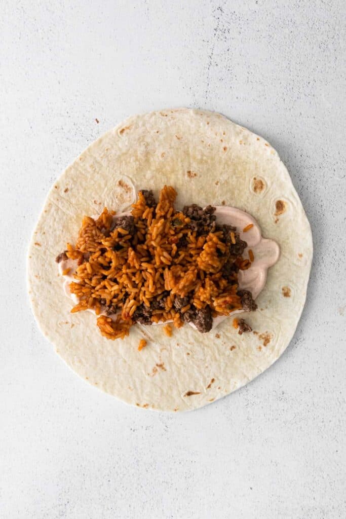 Sour cream, ground beef, and Spanish rice on a tortilla. 