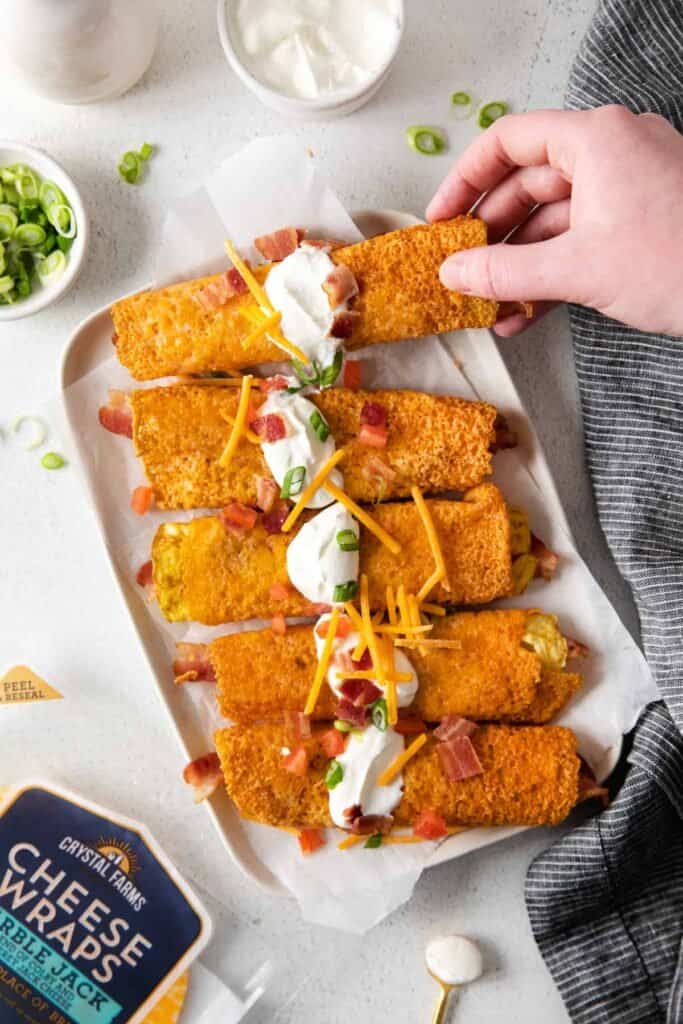 bacon and egg breakfast taquitos on a plate topped with sour cream