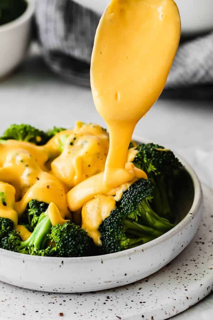 Drizzling cheese sauce over broccoli. 