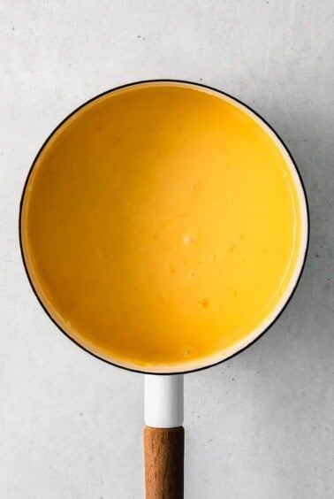 Cheese sauce simmering in a pan with a wooden spoon.