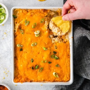 a person dipping a tortilla chip into a casserole dish.
