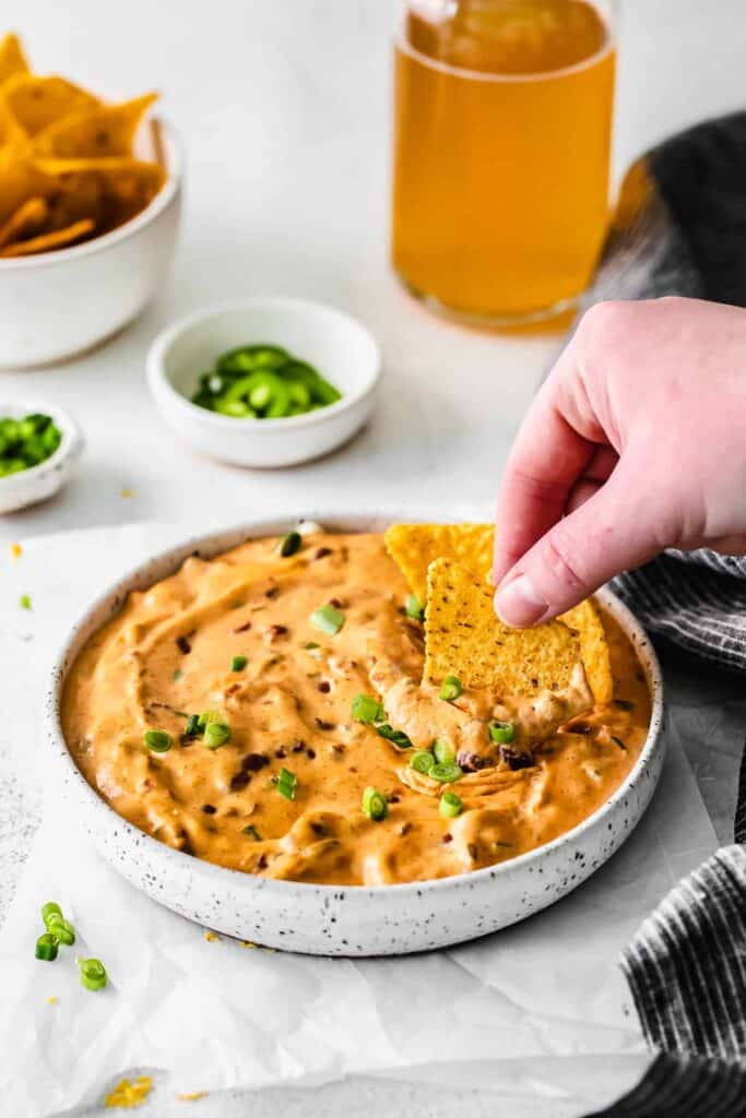a tortilla chip being dipped into chili cheese dip 