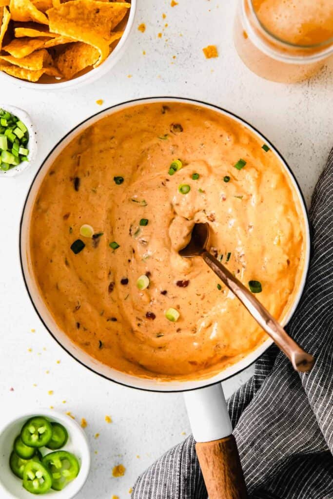 chili cheese dip in a sauce pan topped with fresh green onion