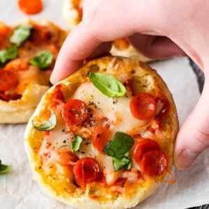 a hand is holding a small pizza on a baking sheet.