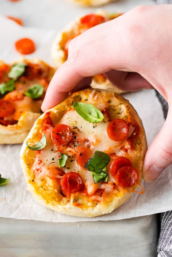 a hand is holding a small pizza on a baking sheet.