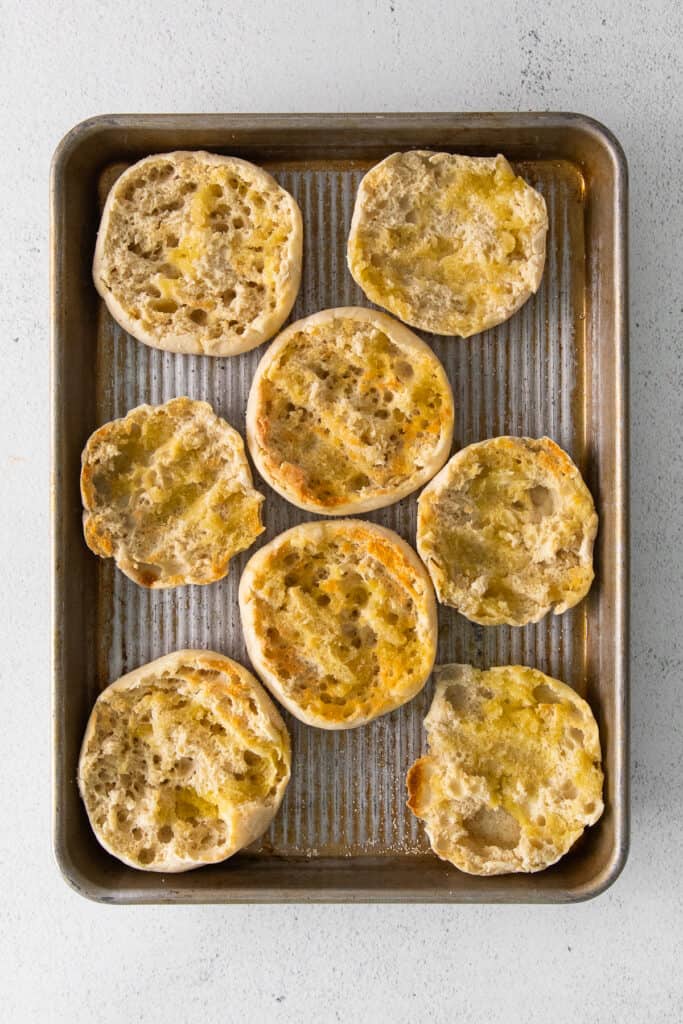 Toasted english muffins on a baking sheet.