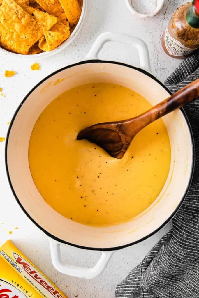 velveeta cheese sauce in a stock pot with a wooden spoon