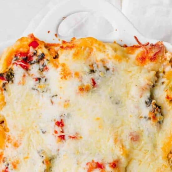 Chicken alfredo lasagna with spinach and cheese in a white baking dish.