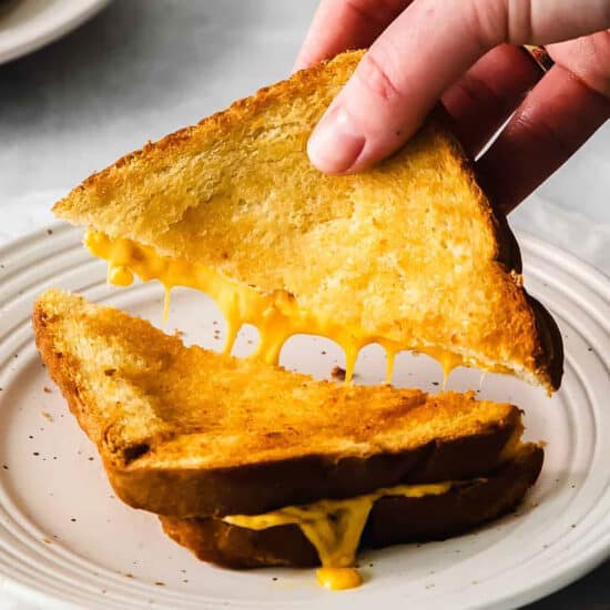A person grabbing a piece of grilled cheese sandwich.