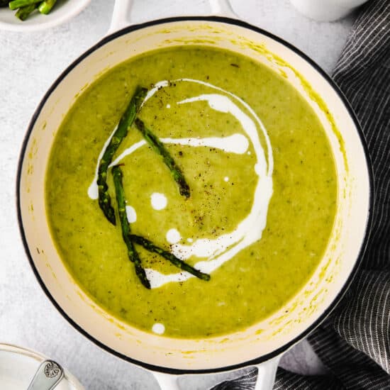 a bowl of green soup with asparagus and sour cream.