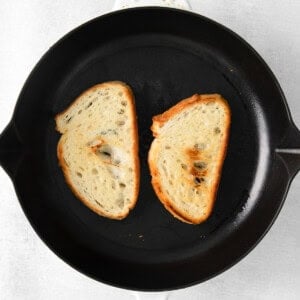 Two slices of mascarpone toast sizzling in a skillet on a white background.