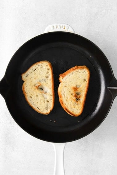 Two slices of mascarpone toast sizzling in a skillet on a white background.