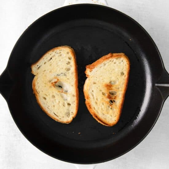Two slices of mascarpone toast sizzling in a skillet on a white background.