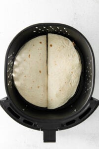 two tortillas in an air fryer on a white background.