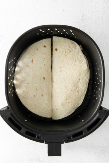 two tortillas in an air fryer on a white background.