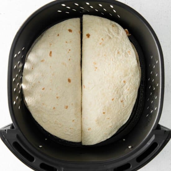 two tortillas in an air fryer on a white background.