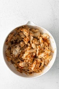 shredded chicken in a white bowl on a white surface.