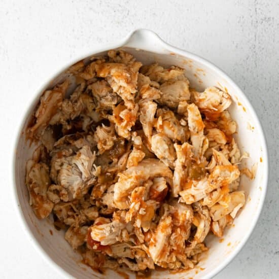 shredded chicken in a white bowl on a white surface.