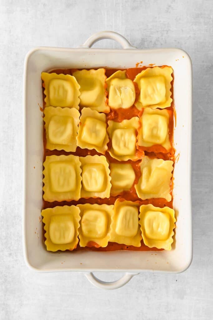 Layering baked ravioli and sauce in a casserole dish. 