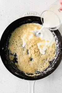 a person pouring milk into a frying pan.