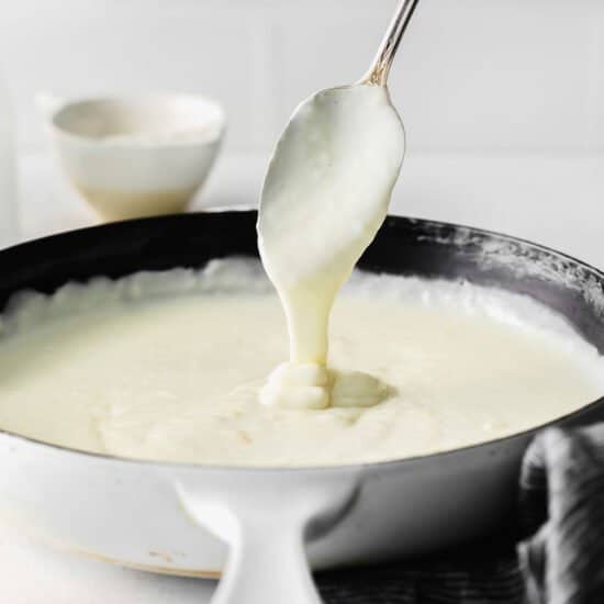 spoon dripping white sauce into pan.